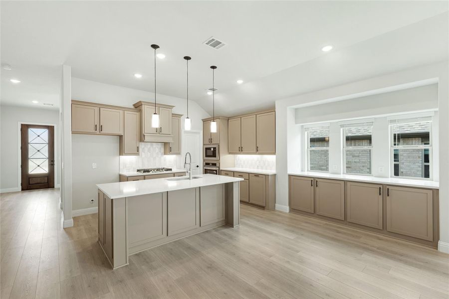Kitchen with large center island, tan cabinets, pendant lights, and light hardwood floors