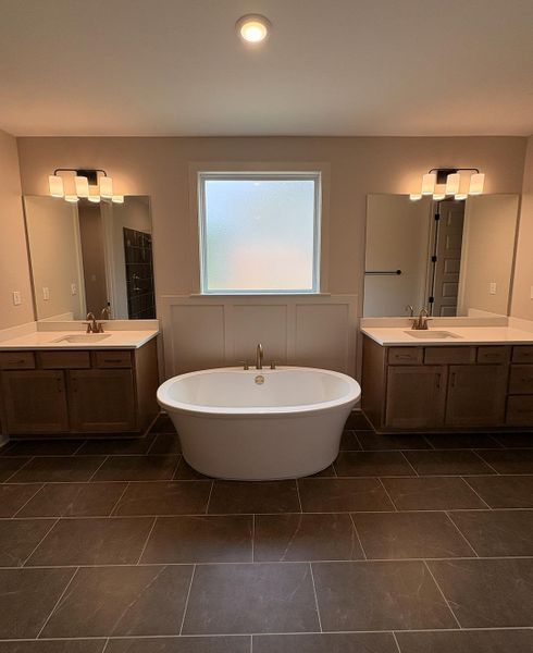 Freestanding soaking tub with brushed brass fixtures, complemented by dual vanities featuring light-colored countertops and wood cabinetry