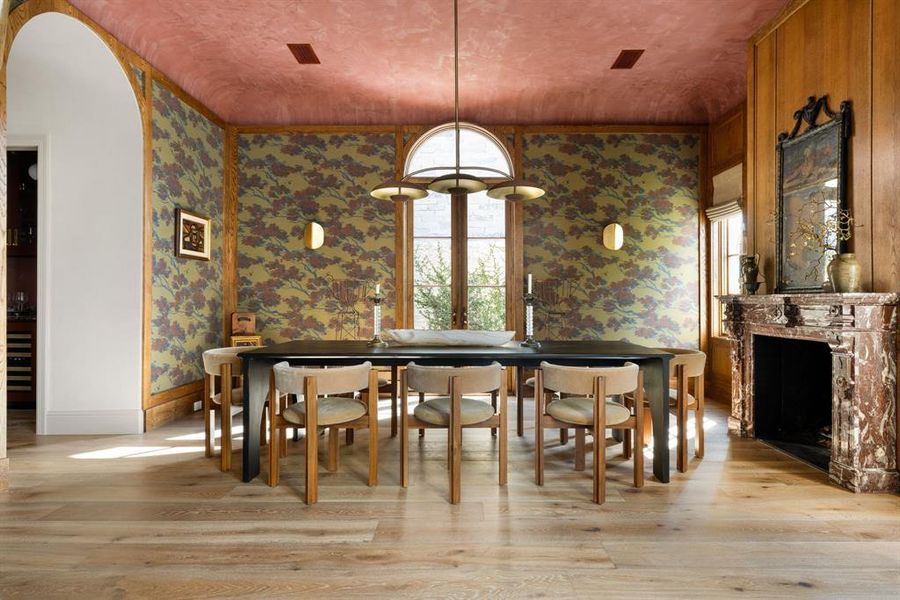 Dining room featuring light wood-style flooring, wallpapered walls, and a high end fireplace