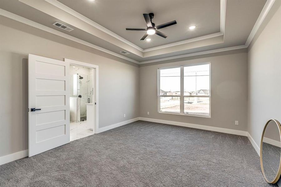 Unfurnished bedroom featuring a tray ceiling, visible vents, carpet floors, and crown molding