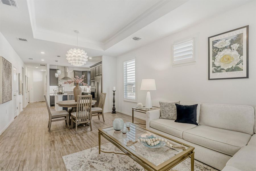 Living area featuring light wood-style flooring, hanging lights, and a tray ceiling