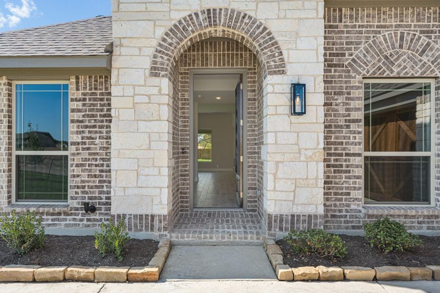 Home entrance with arched stone and brick surround, gray front door, and wall sconce light fixture