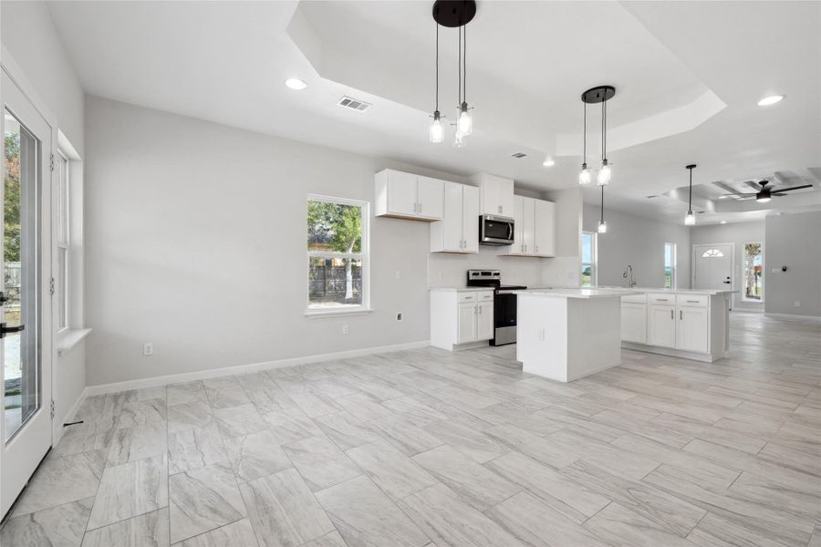 Kitchen featuring a tray ceiling, stainless steel appliances, open floor plan, a center island, and recessed lighting Kitchen featuring a tray ceiling, stainless steel appliances, open floor plan, a center island, and recessed lighting