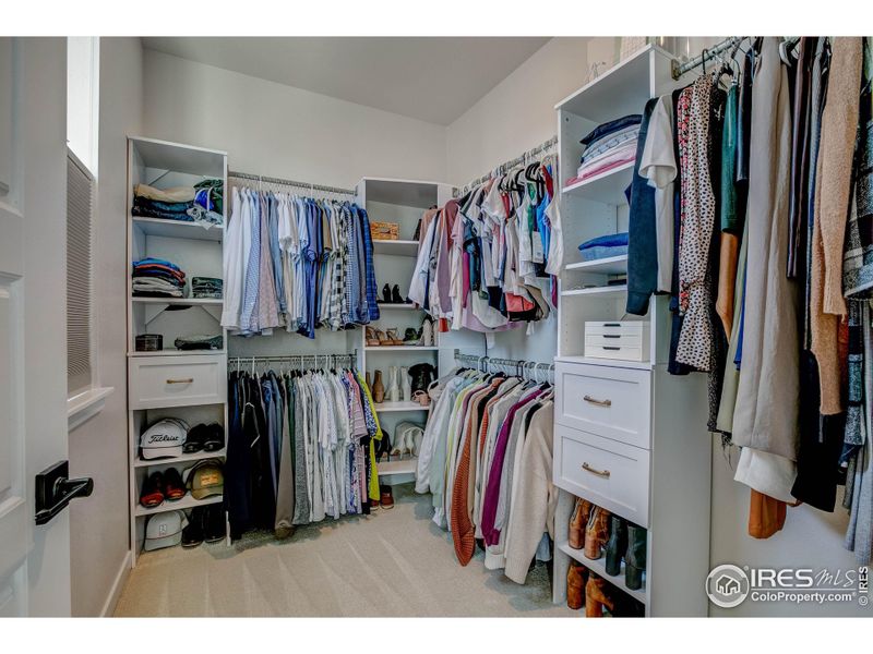 Primary walk-in closet with custom built-in cabinets and a window for natural light.