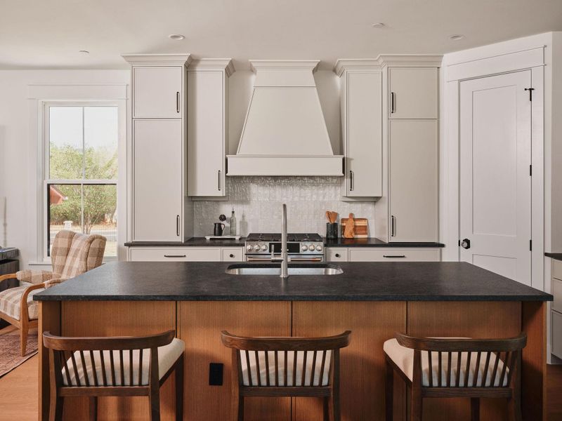 Kitchen featuring a kitchen breakfast bar, a kitchen island with sink, tasteful backsplash, dark wood-style flooring, and gas range