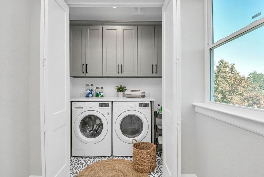 Convenient upstairs laundry with built-in cabinetry, stylish tile flooring, and ample storage space.