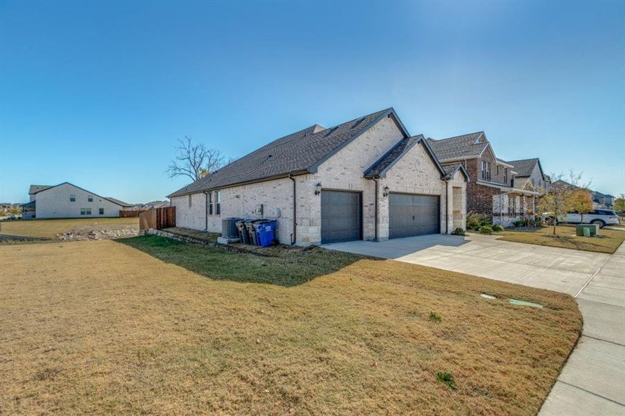 View of side of property with a yard, brick siding, driveway, and an attached garage