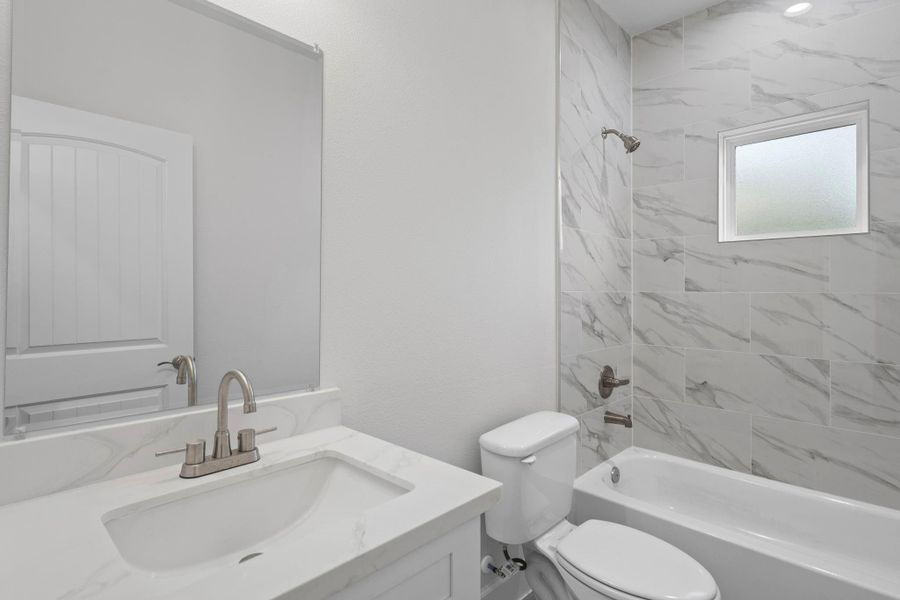 Secondary bathroom with brand new quartz countertops, tile walls, recessed lighting, and a shower/tub combo.