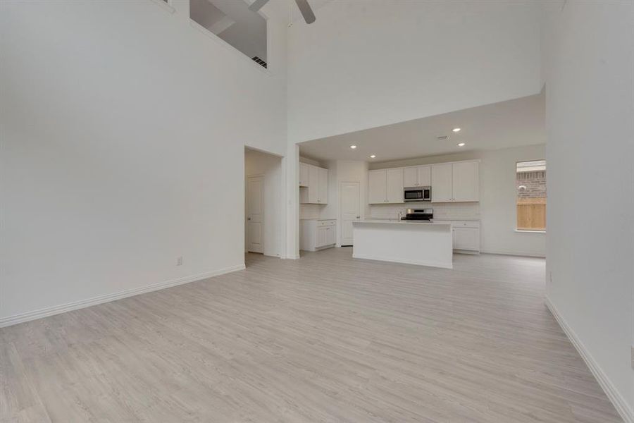 Unfurnished living room featuring ceiling fan, light wood-type flooring, and a towering ceiling