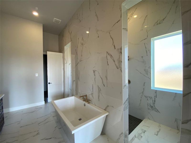 Full bath with light marble finish flooring, a freestanding tub, vanity, healthy amount of natural light, and recessed lighting