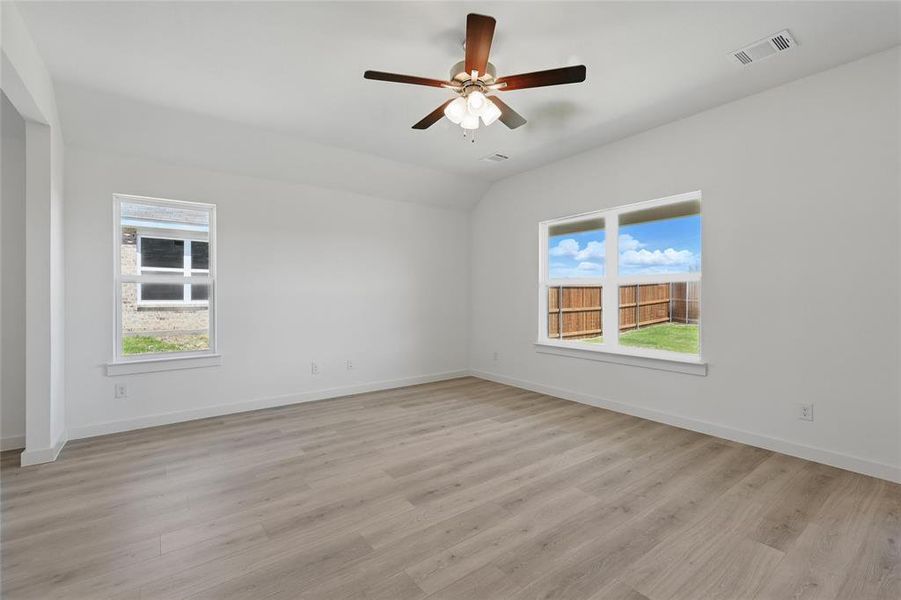 Empty room with baseboards, visible vents, lofted ceiling, light wood finished floors, and ceiling fan Empty room with baseboards, visible vents, lofted ceiling, light wood finished floors, and ceiling fan