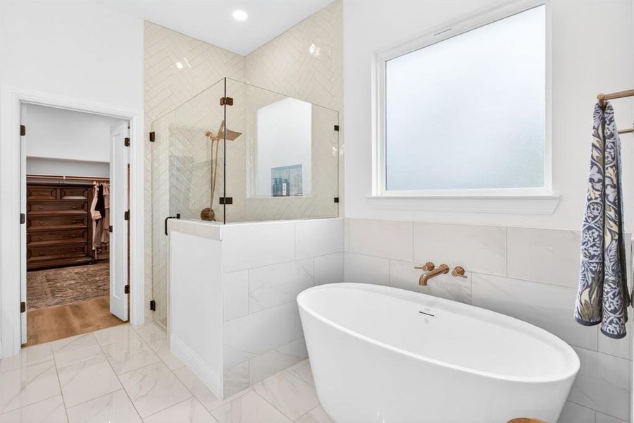 Bathroom featuring a shower stall, a freestanding bath, a spacious closet, tile walls, and marble look tile flooring Bathroom featuring a shower stall, a freestanding bath, a spacious closet, tile walls, and marble look tile flooring