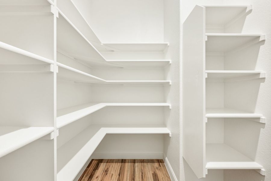 Walk-in pantry with white built-in shelving on three walls and hardwood floors Walk-in pantry with white built-in shelving on three walls and hardwood floors