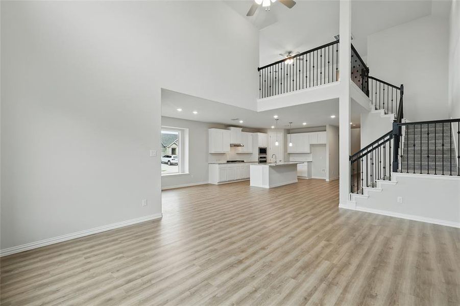 Unfurnished living room featuring light wood-style flooring, a ceiling fan, stairs, a sink, and a towering ceiling Unfurnished living room featuring light wood-style flooring, a ceiling fan, stairs, a sink, and a towering ceiling