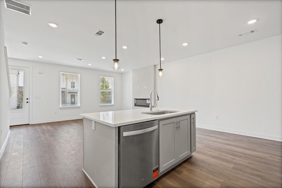 Open-concept living space featuring wood-finish flooring, recessed lighting, and a kitchen island with integrated dishwasher and sink
