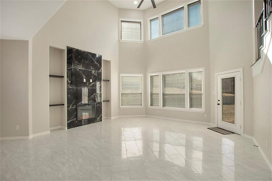 Unfurnished living room featuring healthy amount of natural light, a towering ceiling, and a fireplace Unfurnished living room featuring healthy amount of natural light, a towering ceiling, and a fireplace