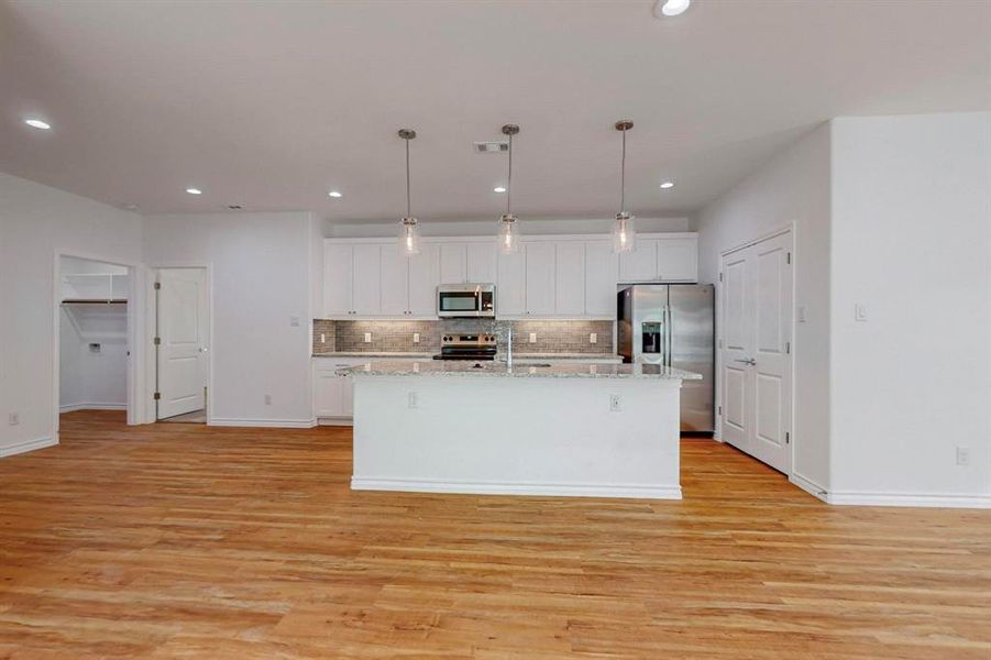 Kitchen featuring white cabinets, appliances with stainless steel finishes, decorative light fixtures, and an island with sink