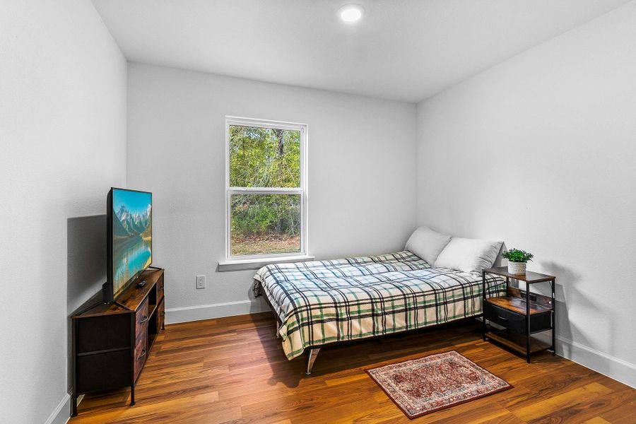 The room has hardwood floors, a window with a view of greenery, and a simple, bright decor.