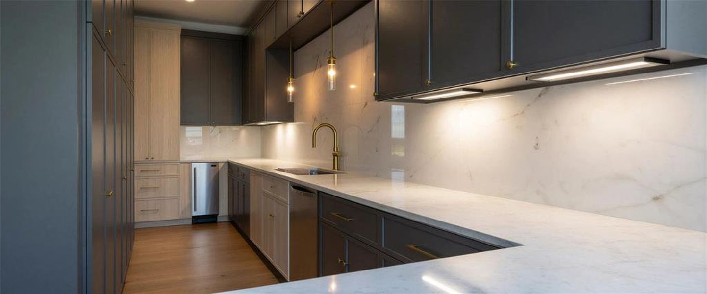 Kitchen featuring open floor plan, gray cabinets, light stone counters, an island with sink, and a glass covered fireplace