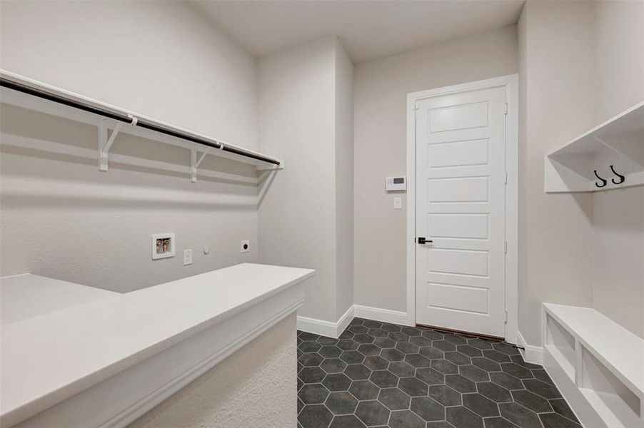 Mudroom and laundry area featuring hexagonal floor tiles, a built-in bench with storage cubbies, and a wall-mounted shelf with coat hooks