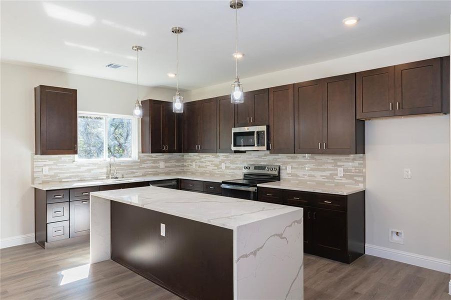 Kitchen featuring stainless steel appliances, light hardwood / wood-style floors, a kitchen island, pendant lighting, and decorative backsplash