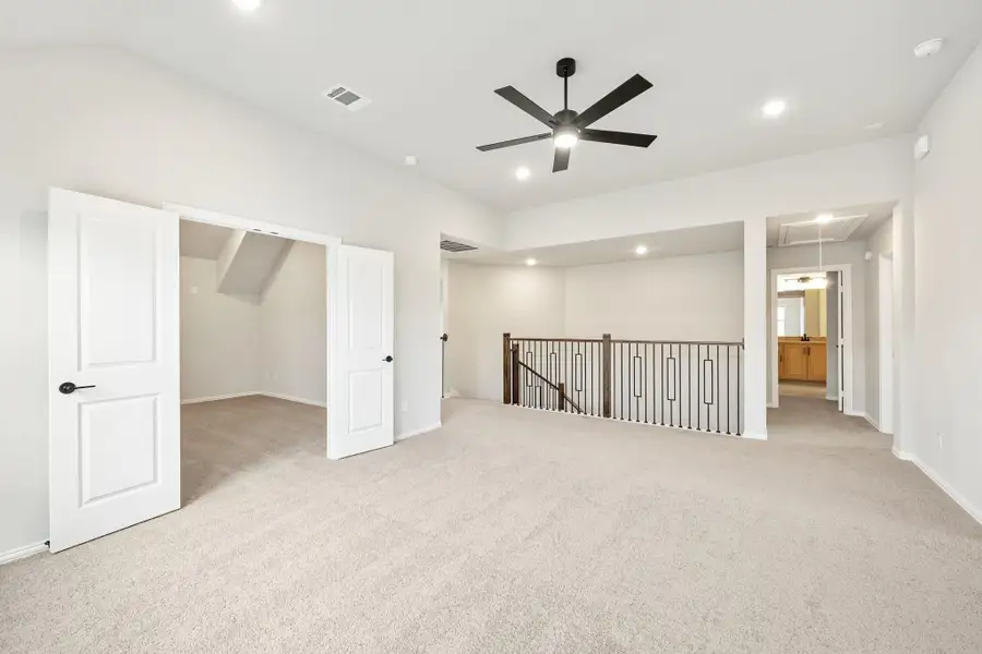 Spacious upstairs loft with carpet, ceiling fan, stair railing, and open doors to closet and bathroom Spacious upstairs loft with carpet, ceiling fan, stair railing, and open doors to closet and bathroom