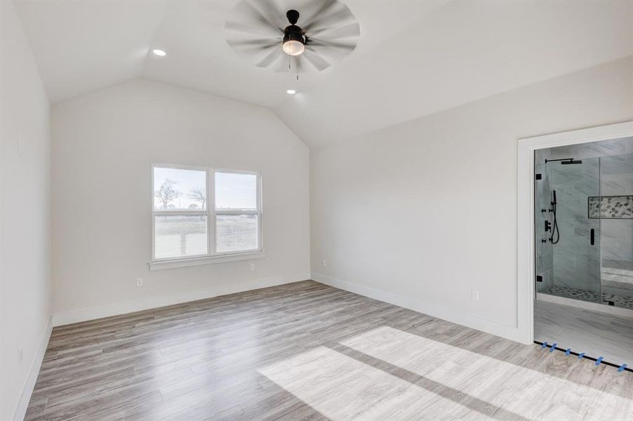 Unfurnished bedroom featuring ceiling fan, light hardwood / wood-style floors, lofted ceiling, and ensuite bathroom