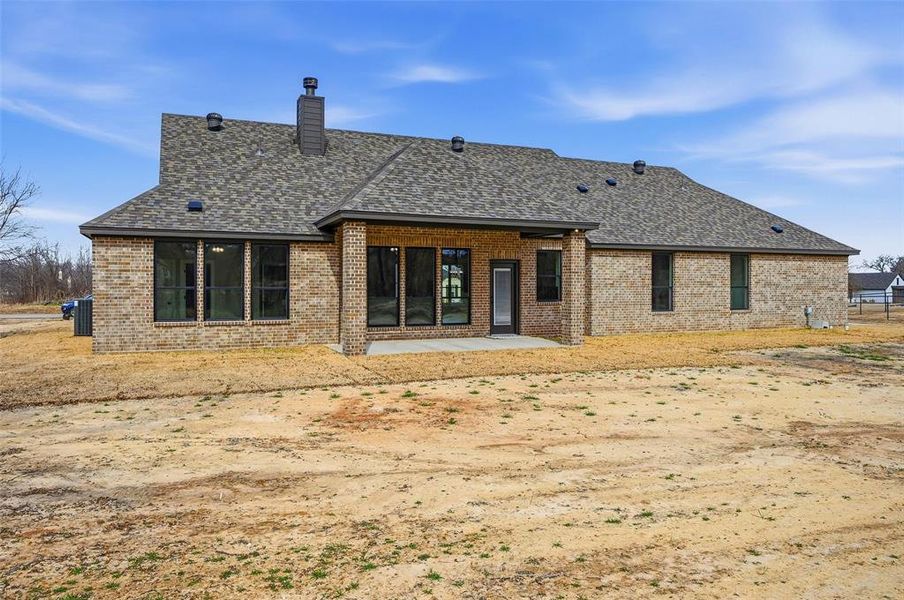 Rear view of property featuring brick siding, a patio area, a shingled roof, and a chimney