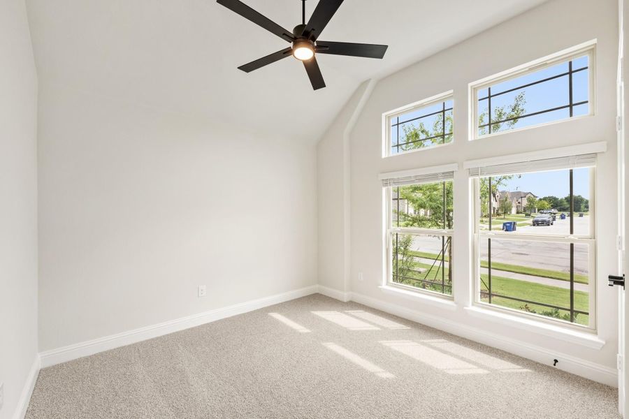 Empty bedroom with vaulted ceiling, ceiling fan, carpet flooring, and large windows with neighborhood view Empty bedroom with vaulted ceiling, ceiling fan, carpet flooring, and large windows with neighborhood view