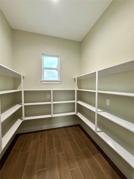 This photo shows a spacious pantry with white shelving on three walls, a small window for natural light, and wood-look tile flooring. Perfect for organized storage.