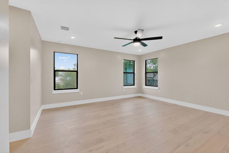 A well-lit bedroom features pristine hardwood flooring and a modern ceiling fan.