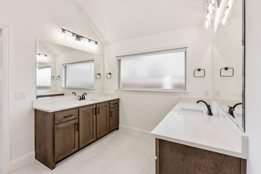 Bathroom with dual vanities, dark wood cabinets, white countertops, and large mirrors with overhead lighting