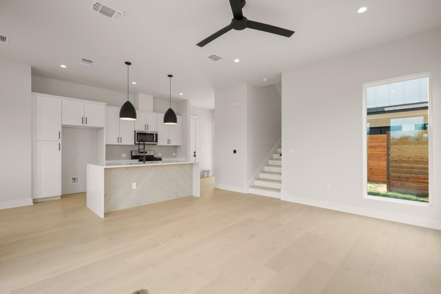 Kitchen featuring white cabinetry, a kitchen island with sink, open floor plan, decorative light fixtures, and light wood finished floors Kitchen featuring white cabinetry, a kitchen island with sink, open floor plan, decorative light fixtures, and light wood finished floors