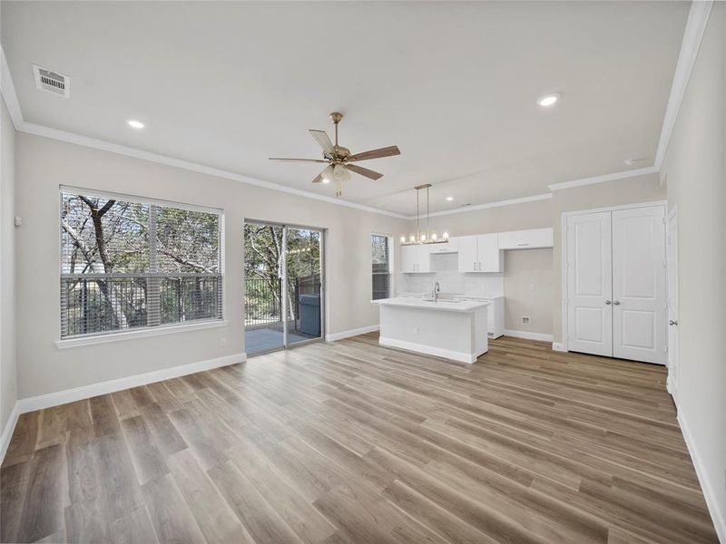 Unfurnished living room featuring ceiling fan with notable chandelier, light wood-style flooring, visible vents, and baseboards