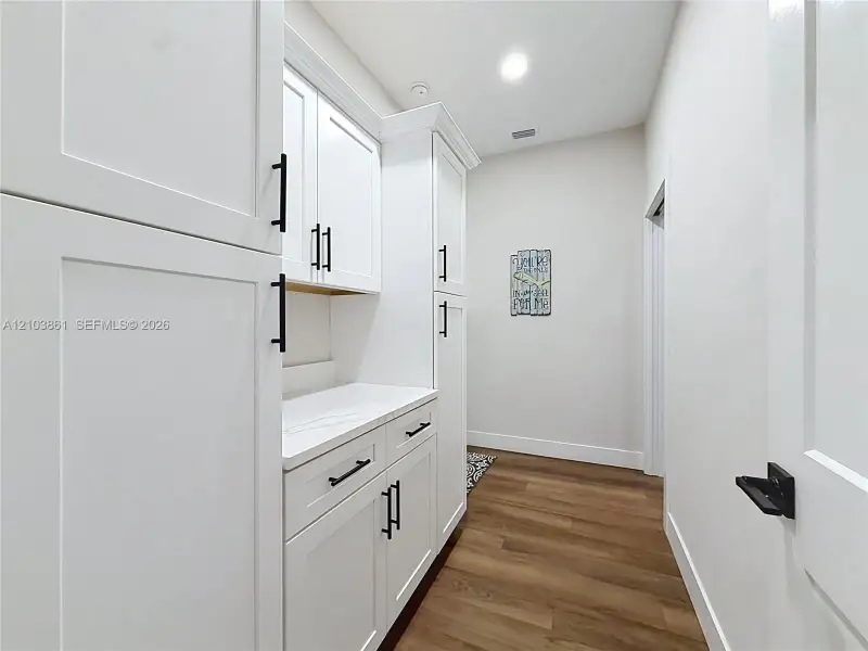 White shaker-style cabinetry with matte black hardware, stone-finish countertops, wood-finish flooring, and recessed ceiling lighting