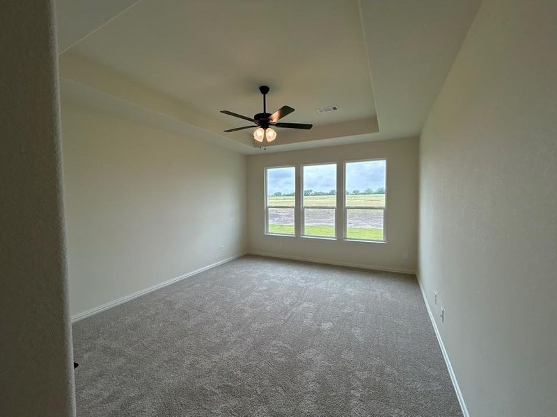 Spacious interior room featuring a tray ceiling with a ceiling fan