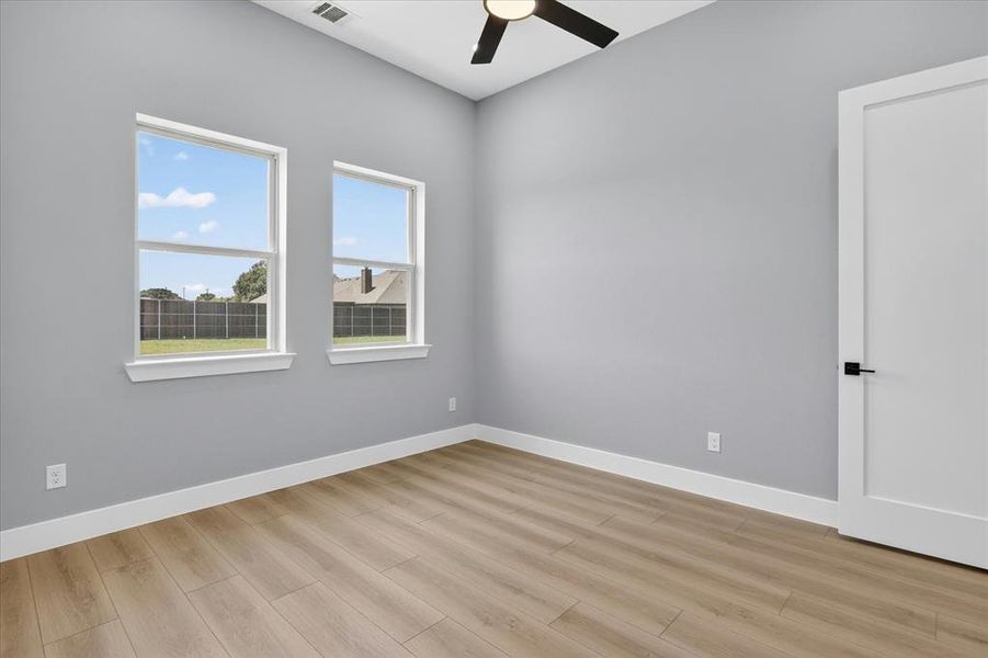 Room featuring wood-finish flooring, two large windows, a ceiling fan, light gray wall paint, and white trim