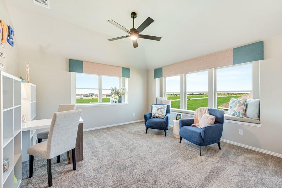 Carpeted sitting room with two blue accent chairs, window seat, ceiling fan, and large windows with outdoor views