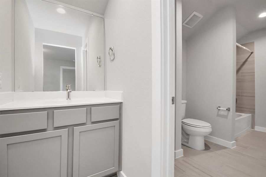 Secondary bathroom, designed for Jack and Jill arrangements, now with a separate vanity area. This well-appointed space showcases stylish tile flooring, a bath/shower combo with an elegant tile surround, and slate colored wood cabinets. Sample photo of completed home with similar floor plan. Actual colors and selections may vary.