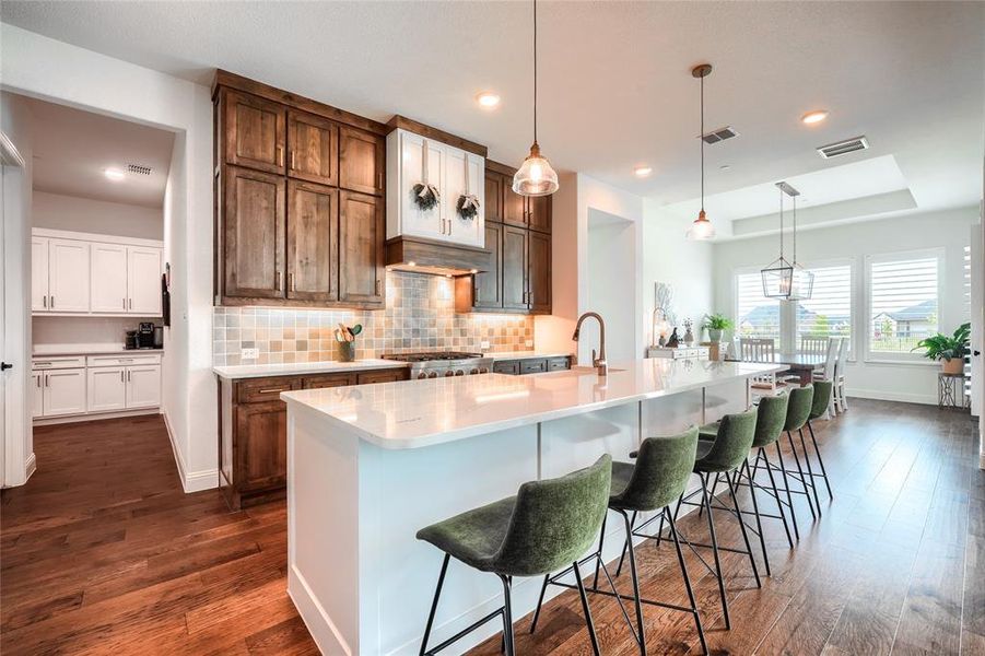 Kitchen with backsplash, decorative light fixtures, a spacious island, a breakfast bar area, and dual tone cabinets
