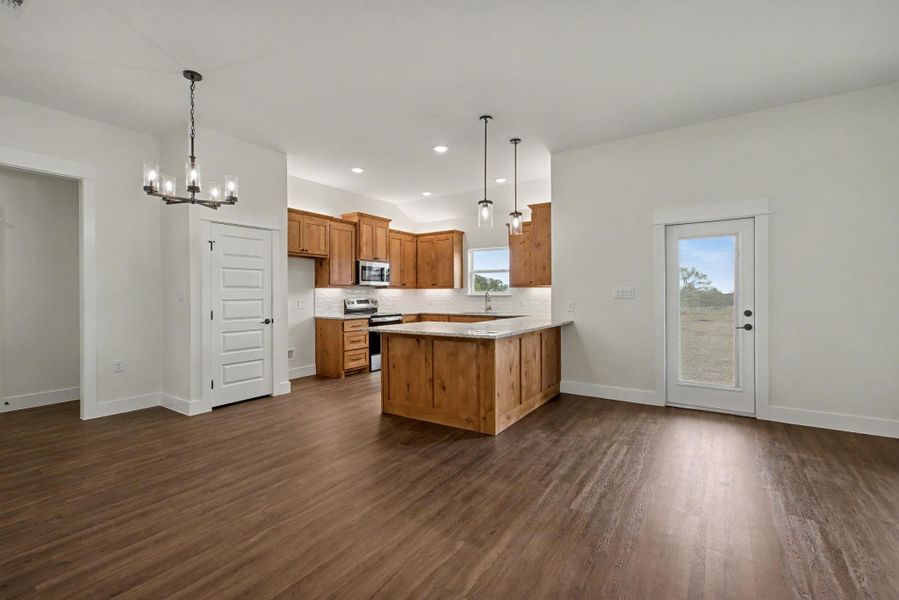 Kitchen featuring wood finish cabinets, a chandelier, a peninsula, stainless steel appliances, and dark wood-style flooring