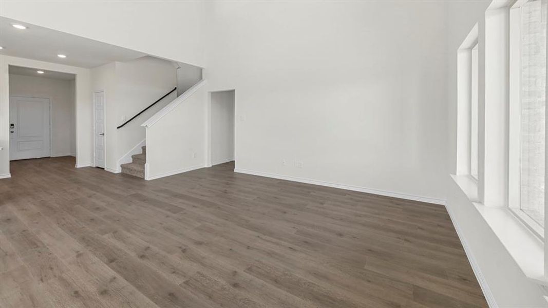 Unfurnished living room featuring wood finished floors, stairway, recessed lighting, and a high ceiling