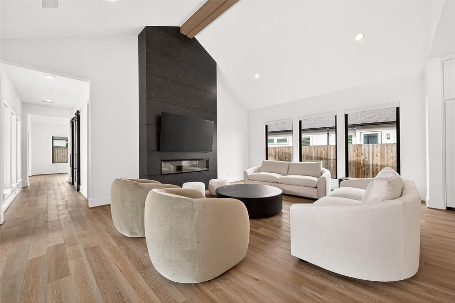 The breathtaking family room serves as the true heart of the home, highlighted by soaring vaulted ceilings with exposed center beam details and a dramatic feature wall showcasing a sleek electric fireplace extending toward the vaulted ceilings. Custom remote window shades throughout the home.