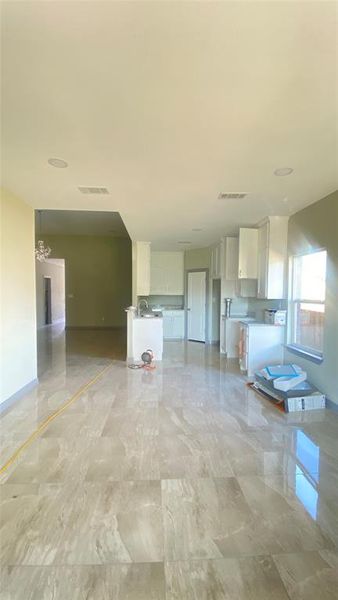 Unfurnished living room featuring an inviting chandelier, sink, and light tile floors