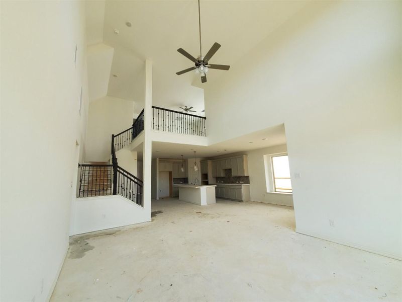 Unfurnished living room featuring stairway, concrete flooring, a high ceiling, and ceiling fan