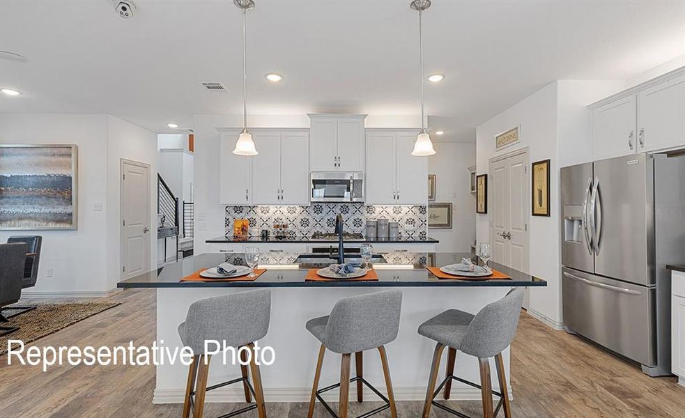 Kitchen featuring a large island with seating, white cabinetry, a decorative tile backsplash, stainless steel appliances, and wood-finish flooring