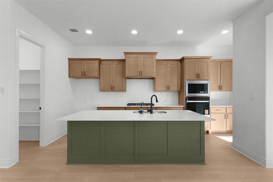 Kitchen with light wood-type flooring, a kitchen island with sink, recessed lighting, stainless steel microwave, and green cabinets