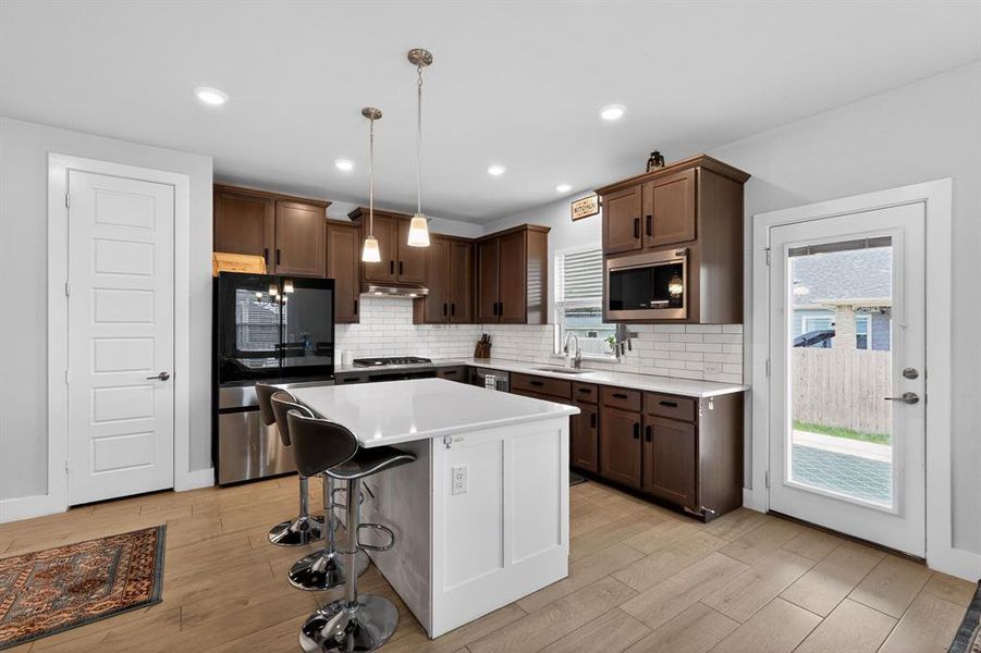 The kitchen features a white island with pendant lighting, rich wooden cabinetry, and stainless steel appliances