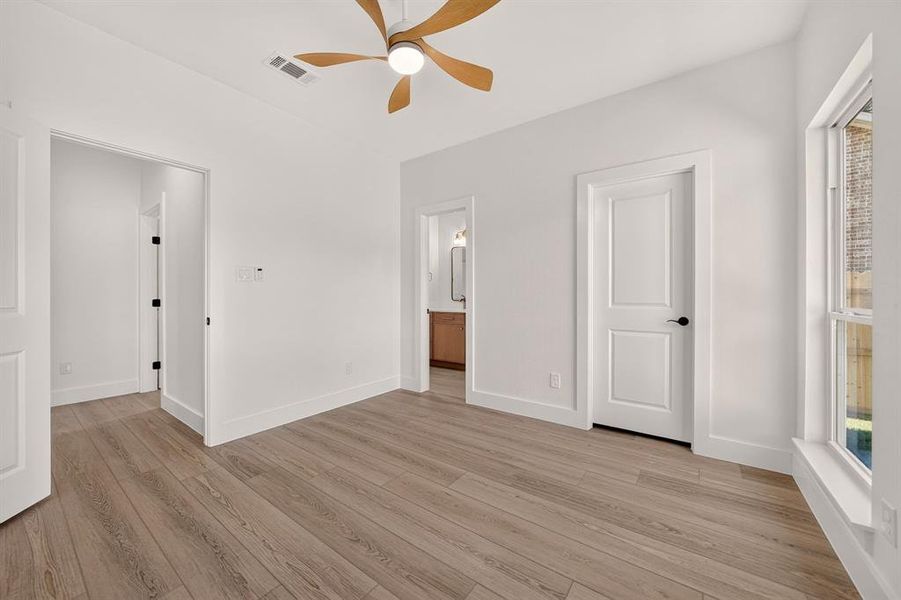 Room featuring wood-finish flooring, a ceiling fan with light fixture, white interior doors, and a window with white trim