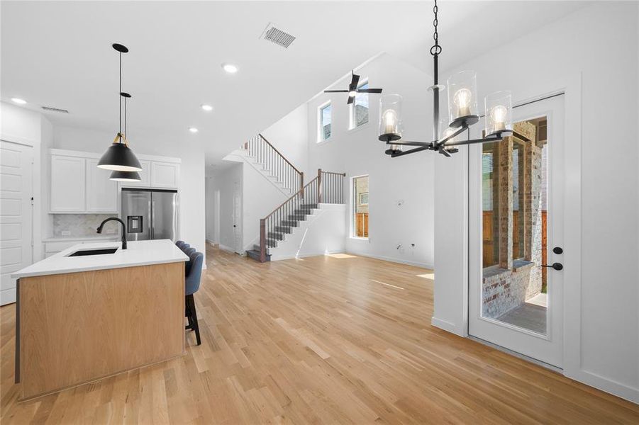 Open-concept interior featuring light wood-finish flooring, a contemporary kitchen island with a light-toned countertop, and a grand staircase with dark wood handrails